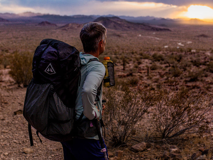 Man on a hike in desert watching sunset