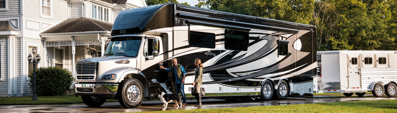 Man, woman and do opening up the door to their new newmar RV that is white and black