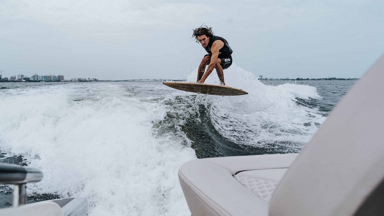 Guy riding the waves being pulled by a Launch 25 GT boat