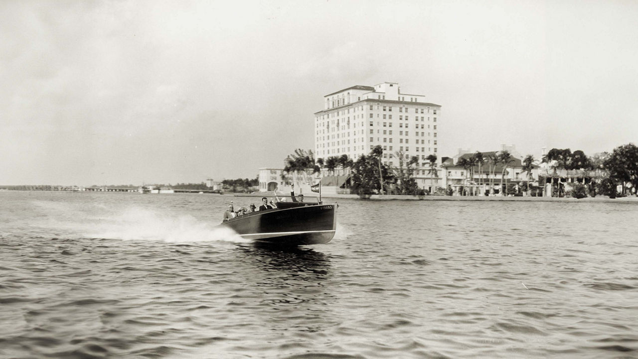 Chris craft boat on the water with a building in the background