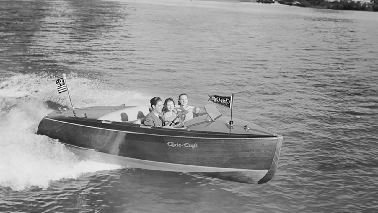 A chris craft boat on the water with 3 people inside