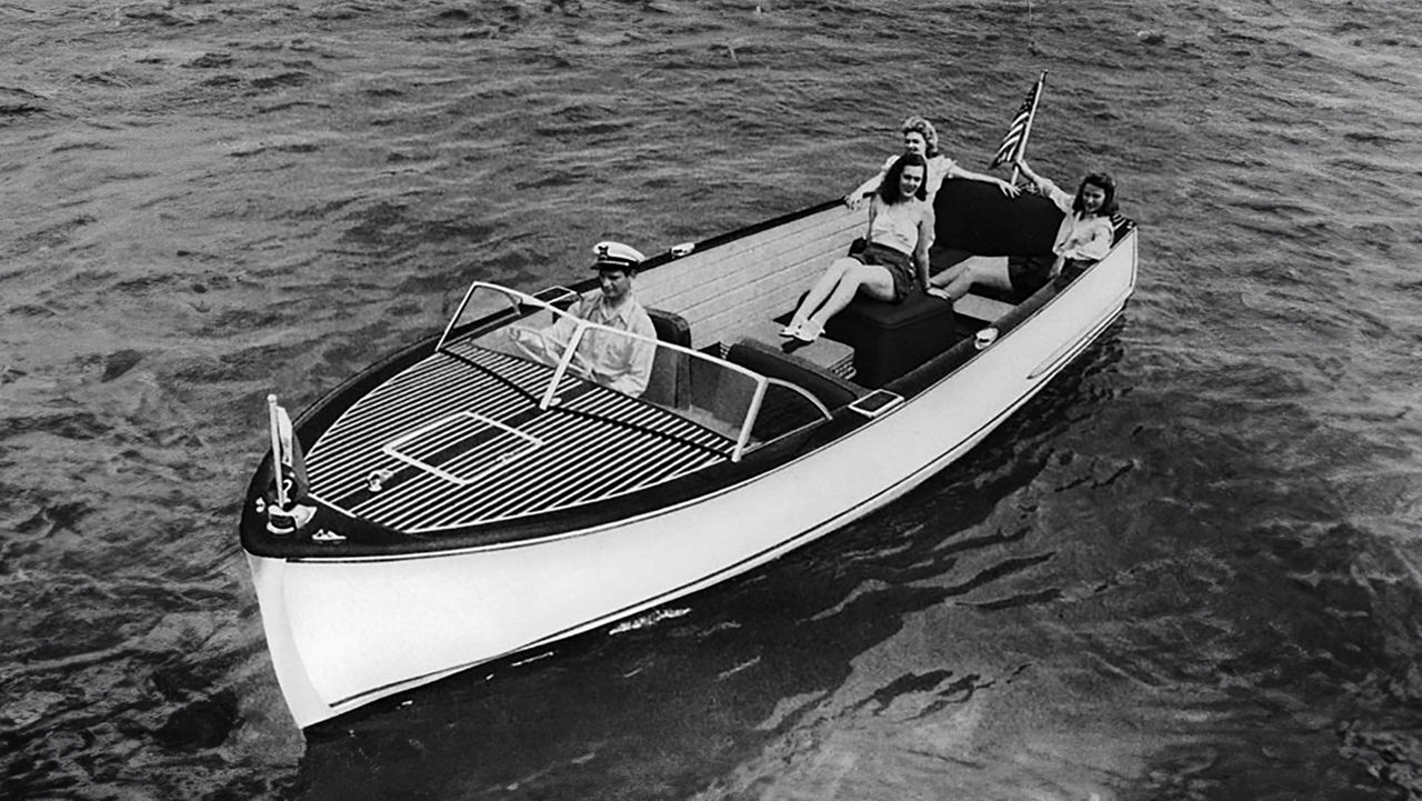 A chris craft boat on the water with four people inside