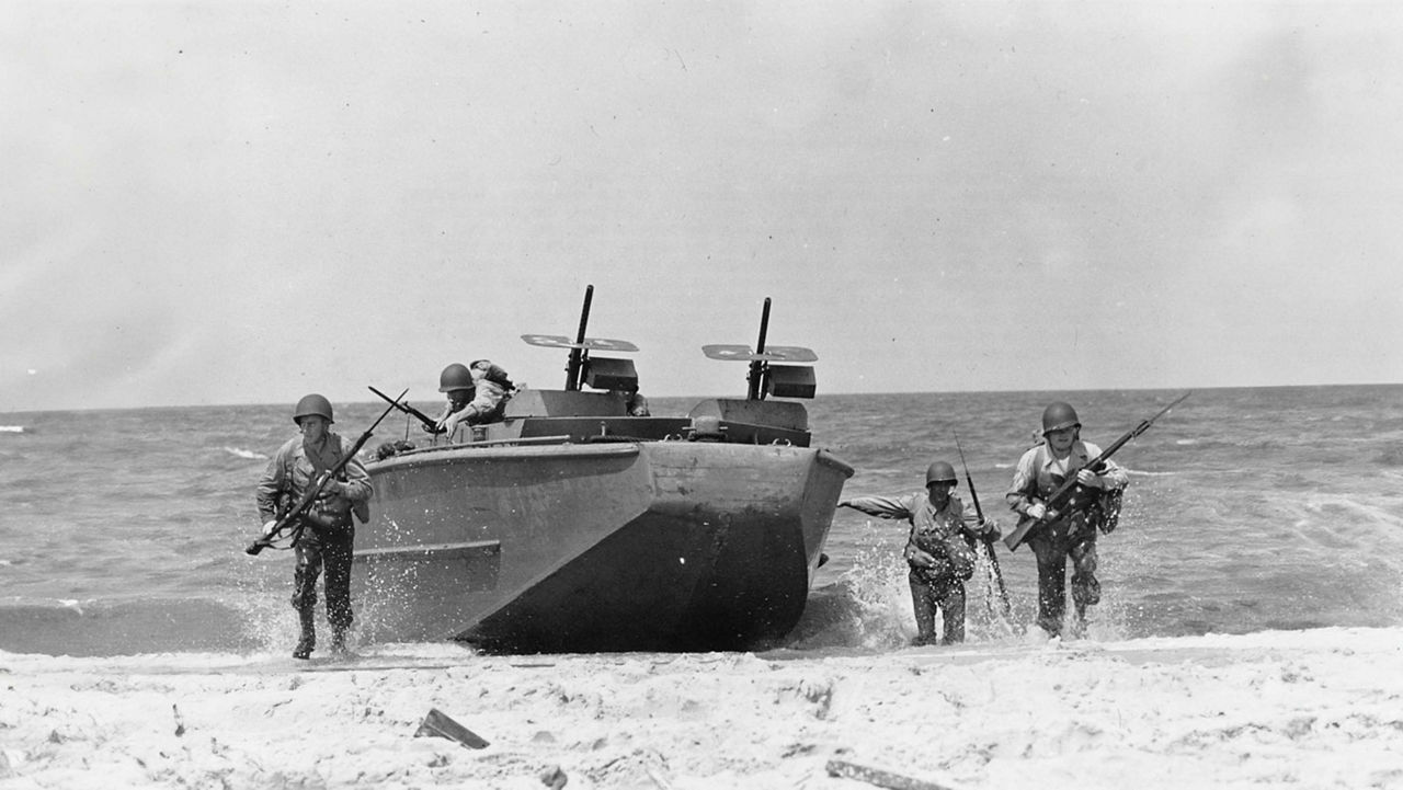 A chris craft boat nearing the shore with soldiers surrounding it