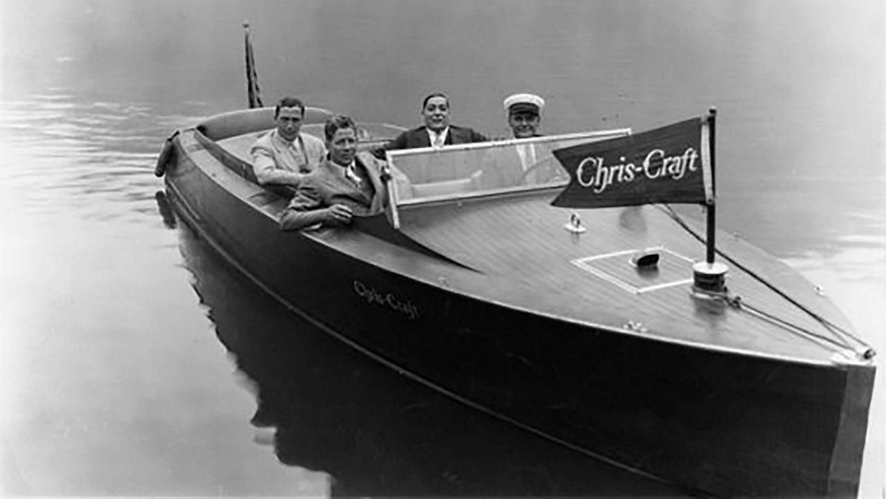 A boat with a chris craft flag with people inside of it