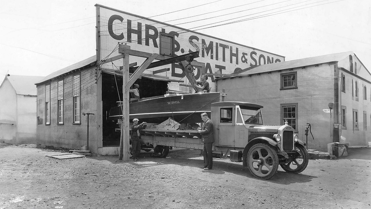 An old fashion car being loaded with a chris craft boat