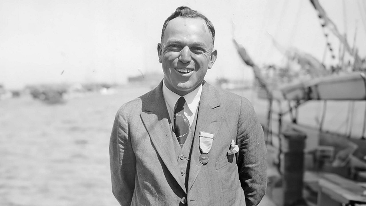 A man in a suit smiling with the ocean behind him