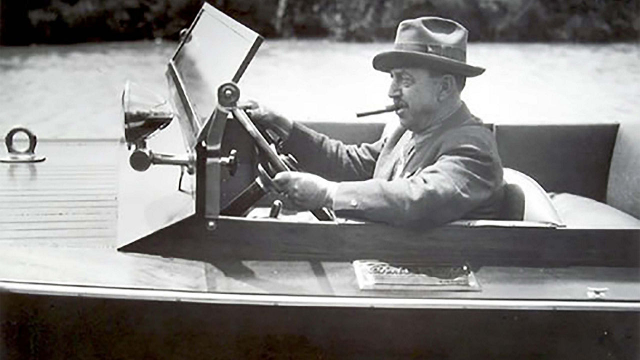 A man with a cigar in his mouth driving a chris craft boat