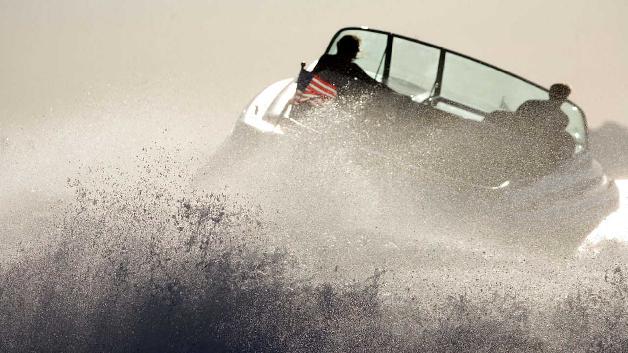 A boat with an american flag on it moving to the right with water splashing behind it