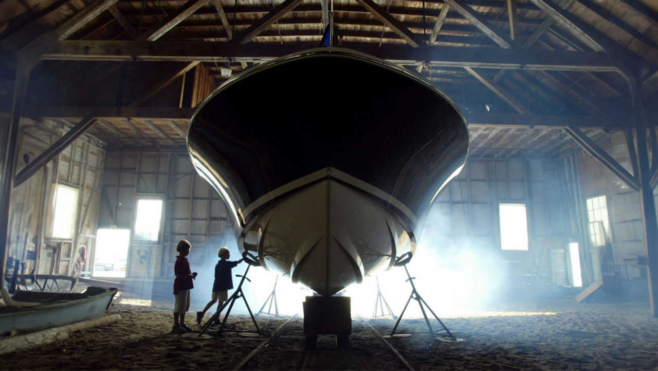 A chris craft boat on stands with two men on the left of it