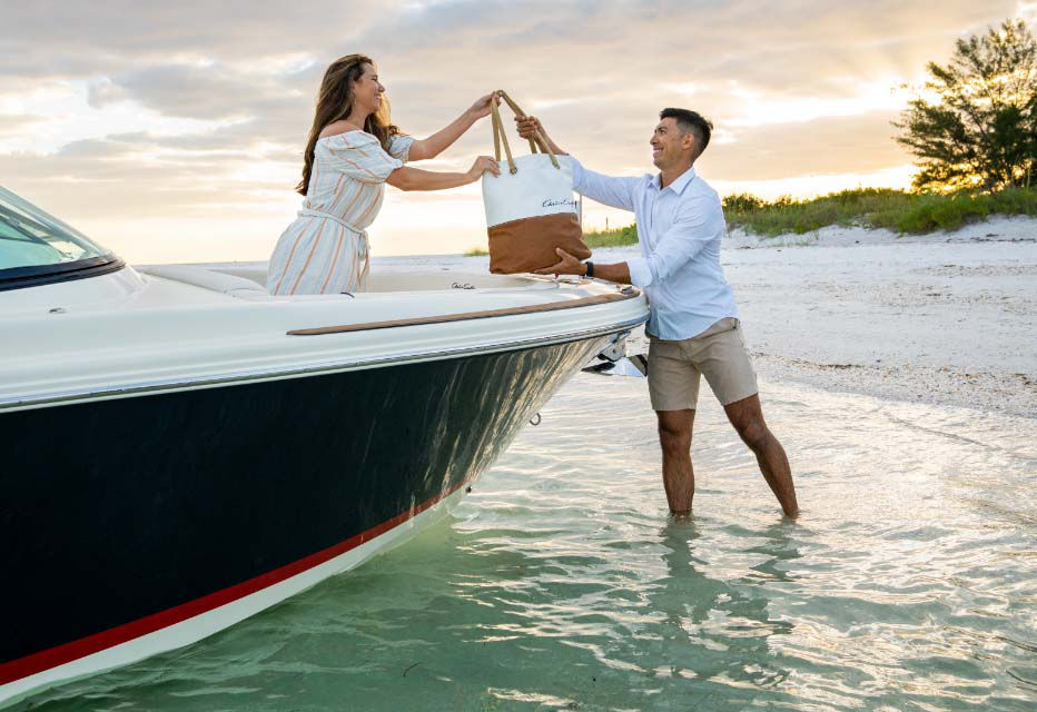Lady on a chris craft boat handing a bag to a man in the water