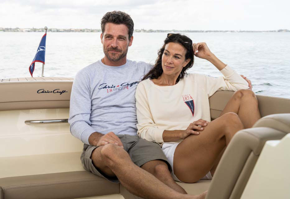 A man and a women sitting in the back of a chris craft boat on the water